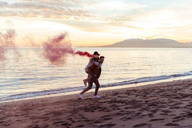 Hombre con mujer con bomba de humo en la orilla del mar