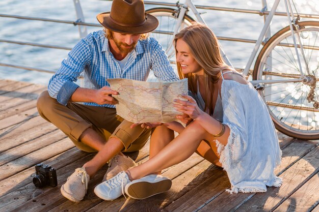 Hombre y mujer con cabello rubio estilo boho hipster moda divirtiéndose juntos, mirando en el mapa turismo