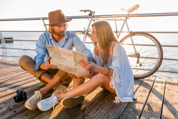 Hombre y mujer con cabello rubio estilo boho hipster moda divirtiéndose juntos, mirando en el mapa turismo