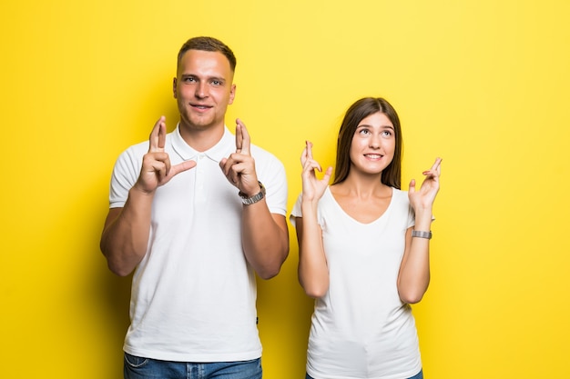 Hombre y mujer en camisetas blancas con los dedos cruzados aislado sobre fondo amarillo