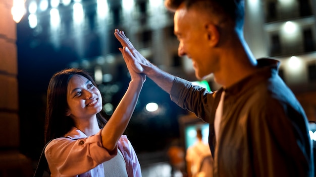 Hombre y mujer chocando los cinco por la noche en las luces de la ciudad