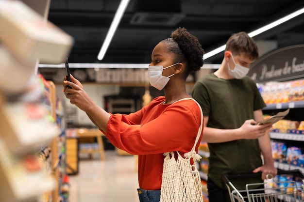 Foto gratuita hombre y mujer comprando en el supermercado mientras usan máscaras médicas