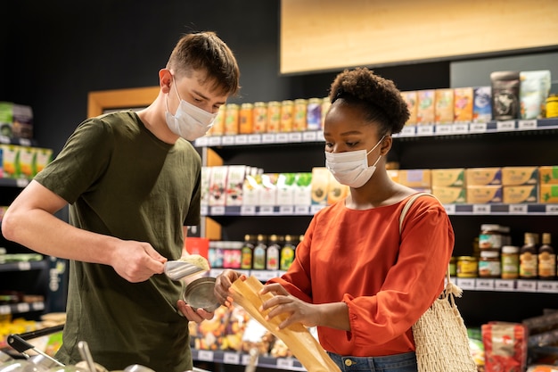 Hombre y mujer comprando en el supermercado mientras usan máscaras médicas