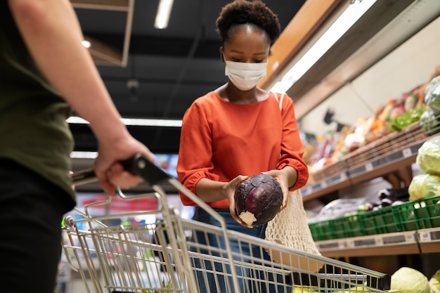 Hombre y mujer comprando en el supermercado mientras usan máscaras médicas