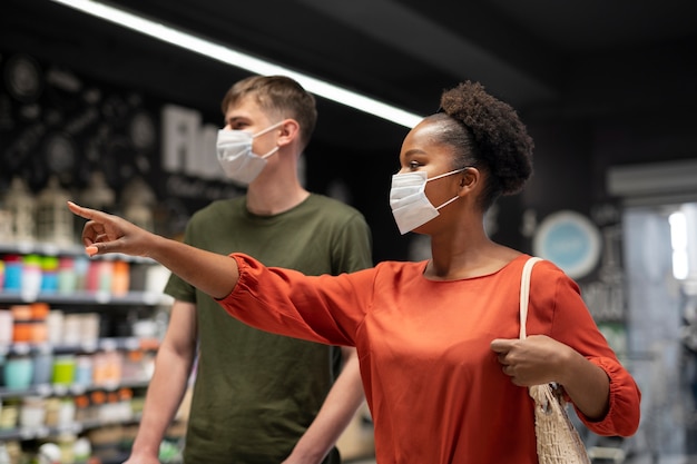 Hombre y mujer comprando en el supermercado mientras usan máscaras médicas