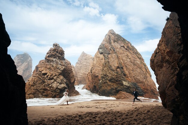 Hombre y mujer corren el uno al otro en la playa entre las rocas