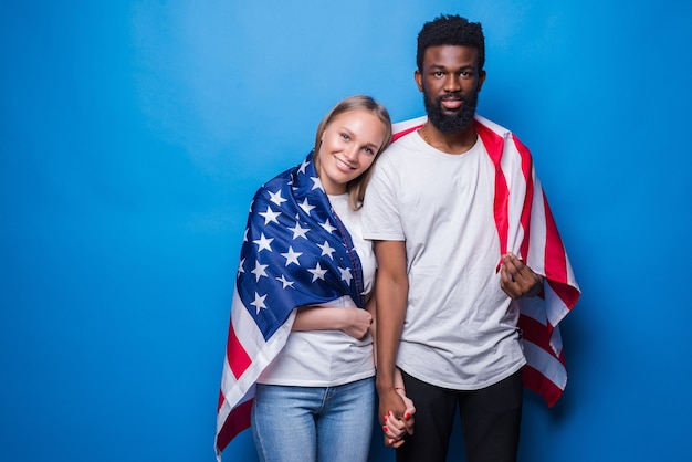 Hombre y mujer cubiertos con bandera americana aislado en la pared azul. Unidad de los estadounidenses.