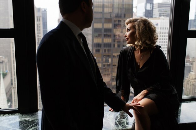 El hombre se para ante una mujer deslumbrante que mira a través de la ventana panorámica en las calles de Nueva York