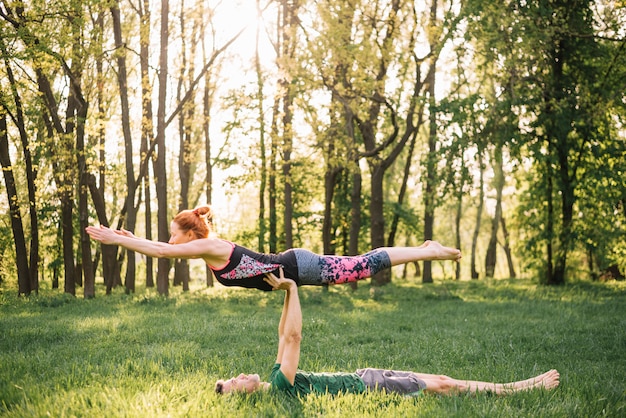 Foto gratuita hombre mujer equilibrada en su mano mientras hacía yoga en campo de hierba