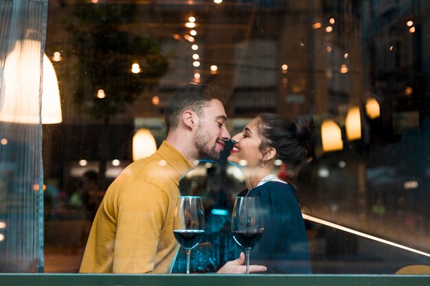 Hombre y mujer felices cerca de copas de vino en restaurante