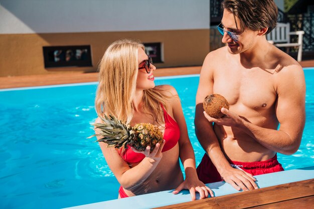 Hombre y mujer con frutas en la piscina