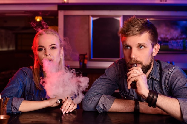 Foto gratuita un hombre y una mujer fumando cigarrillos electrónicos en un bar de vape.