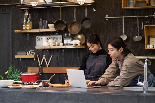 Hombre y mujer japoneses que trabajan usando una computadora portátil en un restaurante