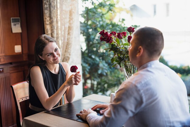 Hombre y mujer joven alegre con la flor que se sienta en la tabla