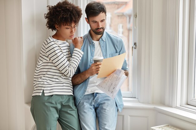 Hombre y mujer joven interracial hacen contabilidad de sus gastos por año, concentrados en el papeleo