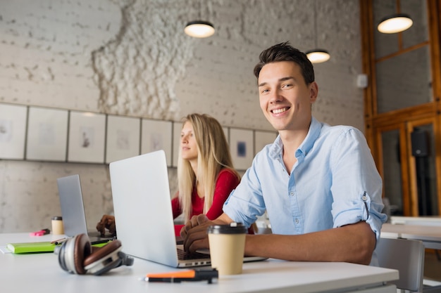 Foto gratuita hombre y mujer joven moderno que trabaja en la computadora portátil en la sala de oficina de coworking de espacio abierto