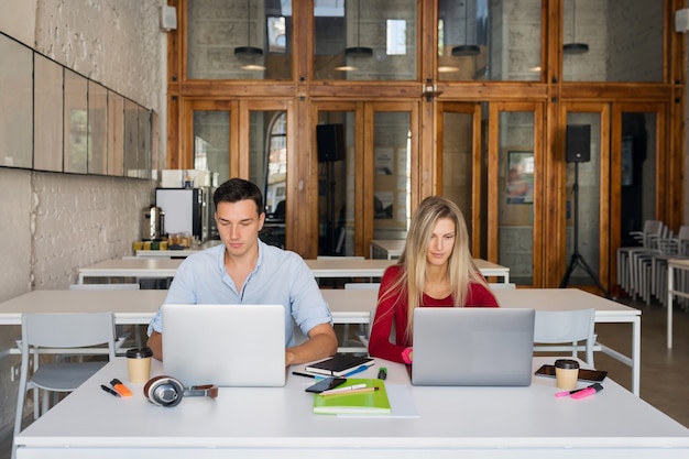 Hombre y mujer joven que trabaja en la computadora portátil en la sala de oficina de coworking