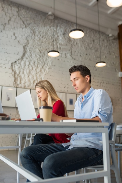 Hombre y mujer joven que trabaja en la computadora portátil en la sala de oficina de coworking