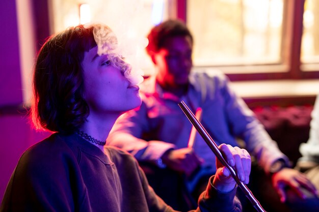 Hombre y mujer joven vaping de una pipa de agua en el interior