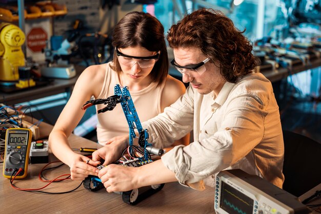 Hombre y mujer jóvenes con gafas protectoras haciendo experimentos en robótica en un robot de laboratorio