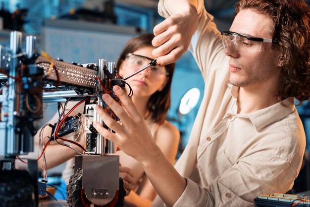 Hombre y mujer jóvenes con gafas protectoras haciendo experimentos en robótica en un robot de laboratorio