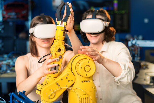 Hombre y mujer jóvenes con gafas VR haciendo experimentos en robótica en un laboratorio Robot sobre la mesa