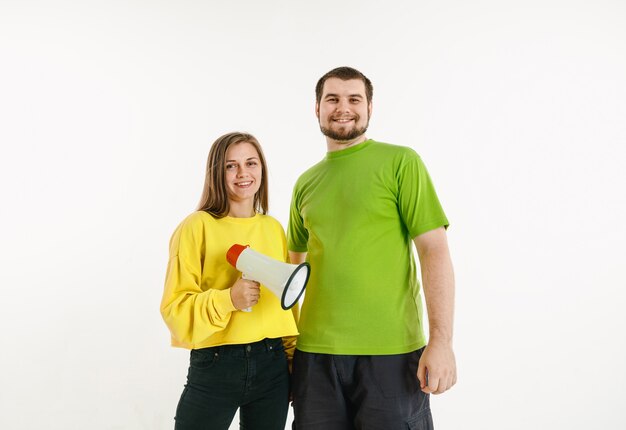 El hombre y la mujer jóvenes lucieron los colores de la bandera LGBT en la pared blanca. Modelos caucásicos con camisas brillantes. Luce feliz, sonriente y abrazado. Orgullo LGBT, derechos humanos y concepto de elección. Sosteniendo la boquilla.