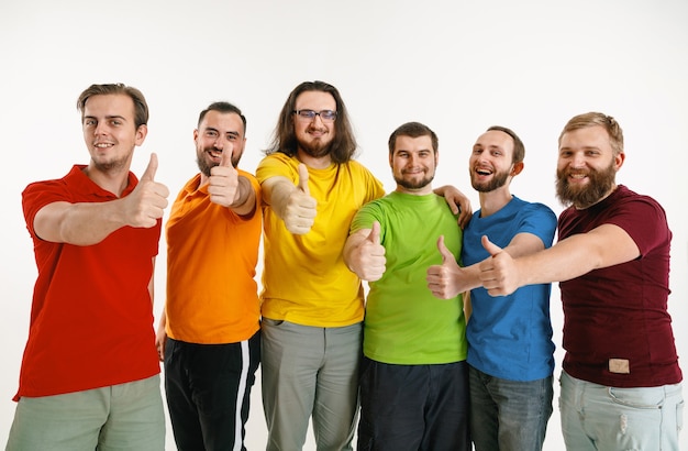 El hombre y la mujer jóvenes vestían los colores de la bandera LGBT en la pared blanca. Modelos caucásicos con camisas brillantes. Lucir felices juntos, sonriendo y abrazándose. Orgullo LGBT, derechos humanos y concepto de elección.