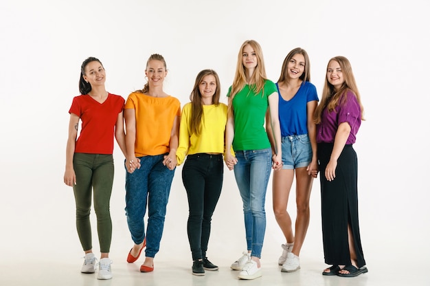 El hombre y la mujer jóvenes vestían los colores de la bandera LGBT en la pared blanca. Modelos caucásicos con camisas brillantes. Lucir felices juntos, sonriendo y abrazándose. Orgullo LGBT, derechos humanos y concepto de elección.