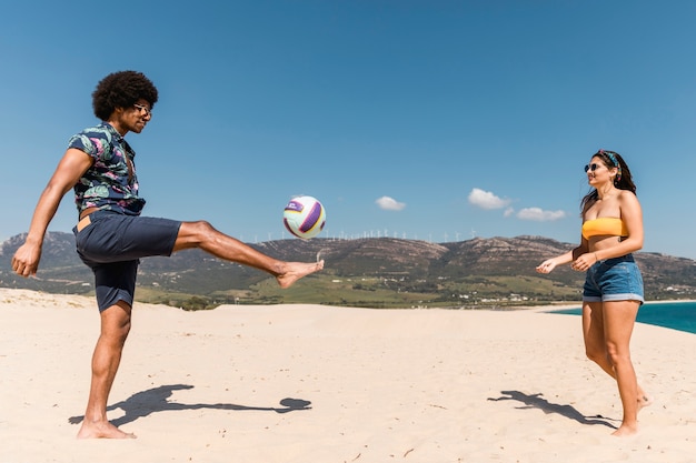 Foto gratuita hombre y mujer jugando al fútbol en la playa de arena