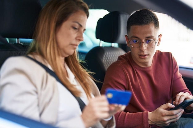 Hombre y mujer madre e hijo usando teléfono inteligente y tarjeta de crédito sentados en el auto en la calle