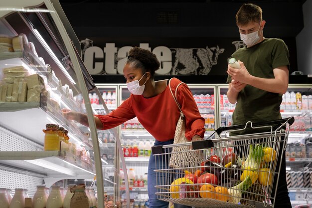 Hombre y mujer con máscaras médicas comprando comestibles con carrito de compras