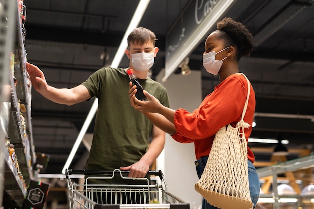 Hombre y mujer con máscaras médicas comprando comestibles con carrito de compras