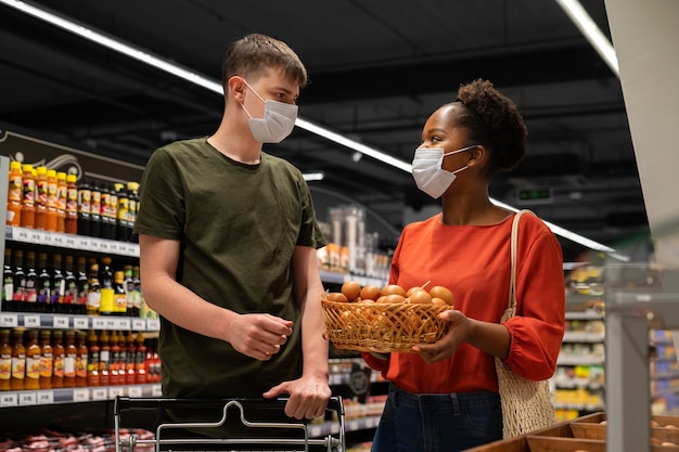 Hombre y mujer con máscaras médicas comprando comestibles con carrito de compras