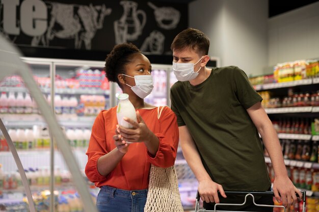 Hombre y mujer con máscaras médicas comprando comestibles con carrito de compras