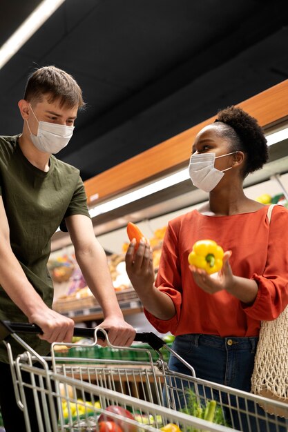 Hombre y mujer con máscaras médicas comprando comestibles con carrito de compras