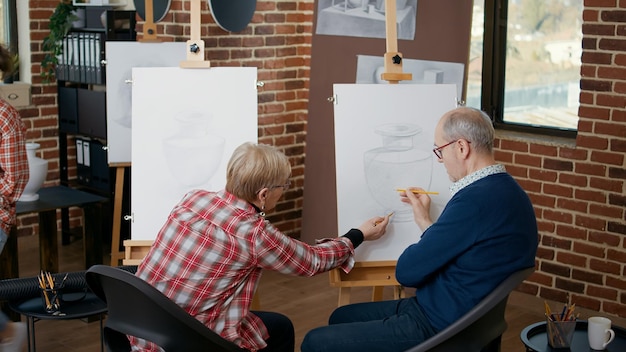 Hombre y mujer mayores en el centro comunitario dibujando un modelo de jarrón sobre lienzo para desarrollar nuevas habilidades. Antiguos estudiantes que asisten a la lección de clase de arte con el maestro para dibujar como resoluciones de año nuevo.