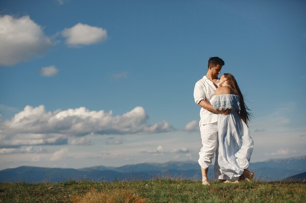 Hombre y mujer en las montañas. Joven pareja de enamorados al atardecer. Mujer con un vestido azul. Peopel de pie sobre un fondo de cielo.