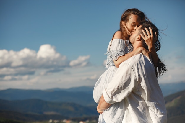 Hombre y mujer en las montañas. Joven pareja de enamorados al atardecer. Mujer con un vestido azul. Peopel de pie sobre un fondo de cielo.