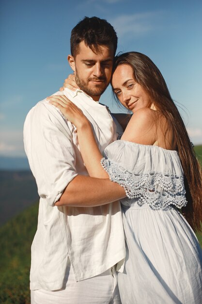 Hombre y mujer en las montañas. Joven pareja de enamorados al atardecer. Mujer con un vestido azul.