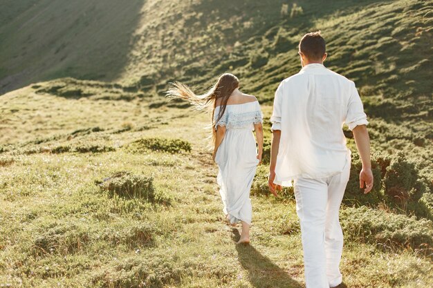 Hombre y mujer en las montañas. Joven pareja de enamorados al atardecer. Mujer con un vestido azul.