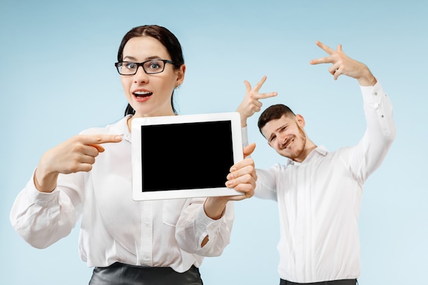 El hombre y la mujer de negocios sorprendidos sonriendo en una pared azul y mostrando la pantalla vacía de la computadora portátil o tableta