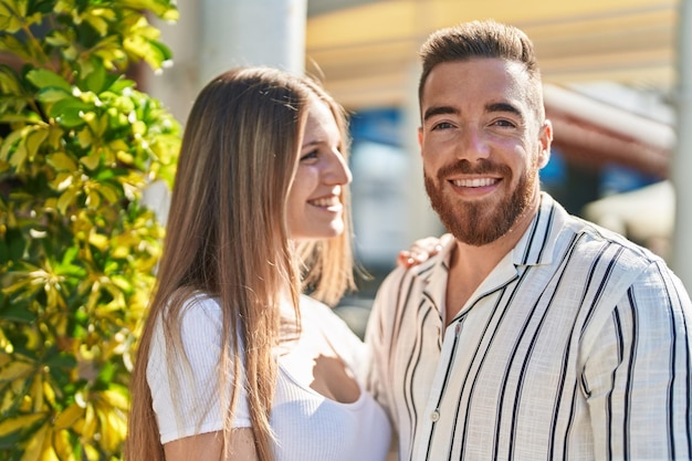 Hombre y mujer pareja sonriendo confiados abrazándose unos a otros en la calle