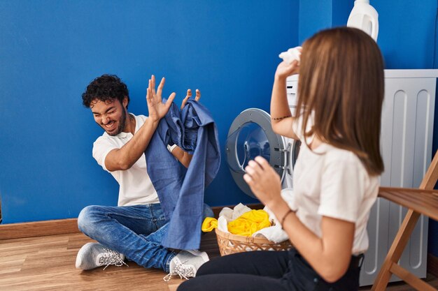 Hombre y mujer pareja sonriendo confiados jugando con ropa de limpieza en la lavandería