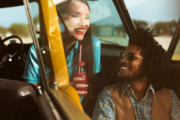 Hombre y mujer posando en estilo retro con auto y bebida