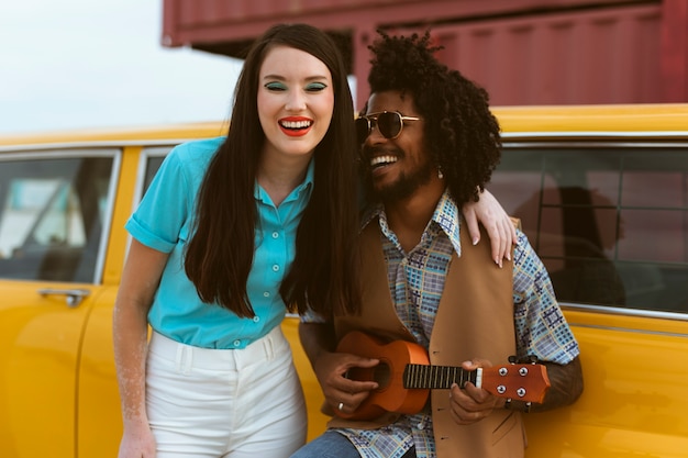 Hombre y mujer posando en estilo retro con coche y ukelele