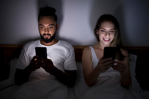 Foto gratuita hombre y mujer revisando su teléfono antes de dormir