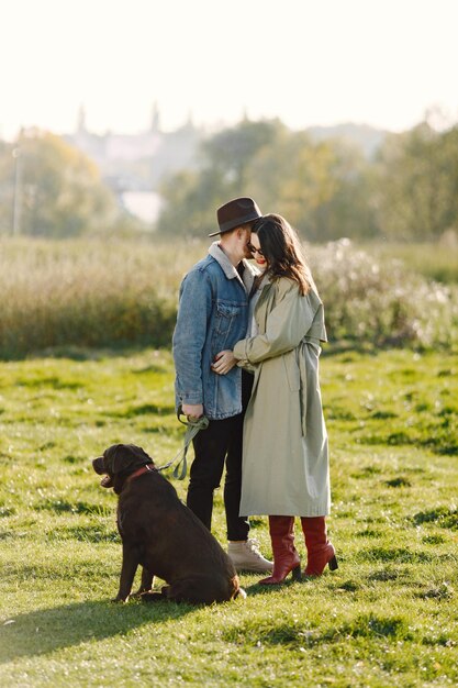 Hombre y mujer en ropa de moda descansando sobre una naturaleza con su labrador. Hombre vestido con chaqueta y sombrero negro y falda de mujer y botas rojas