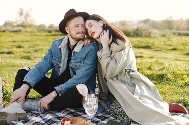 Hombre y mujer en ropa de moda sentado en una naturaleza sobre una alfombra de picnic. Hombre vestido con chaqueta y un sombrero negro y abrigo de mujer