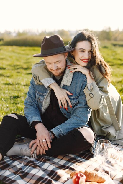 Hombre y mujer en ropa de moda sentado en una naturaleza sobre una alfombra de picnic. Hombre vestido con chaqueta y un sombrero negro y abrigo de mujer